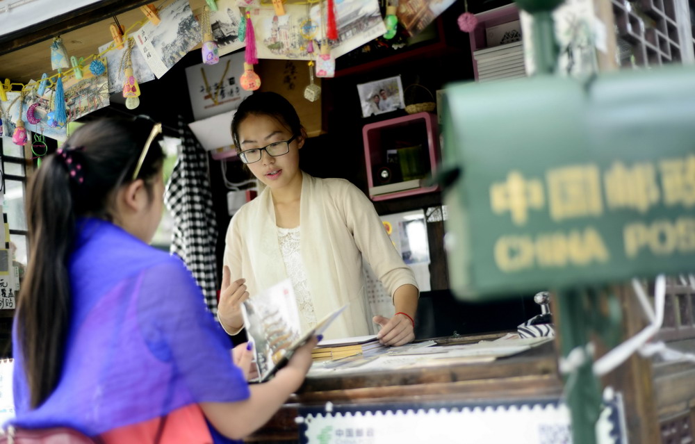済南市の曲水亭街の「済南印象」という名のスタンドで7月8日、お客にハガキを見せる店主の楊帆さん（右）