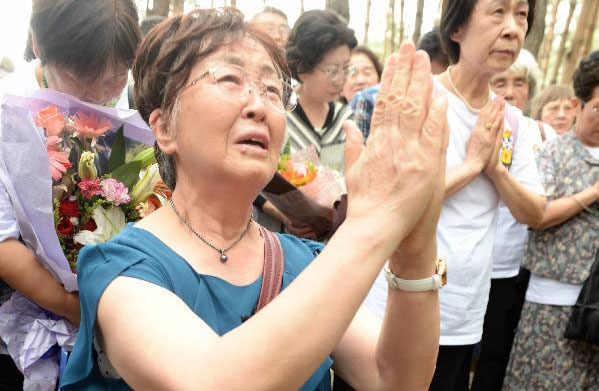中国人養父母の共同墓地の前にひざまずき手を合わせる残留孤児の中春恵子さん 