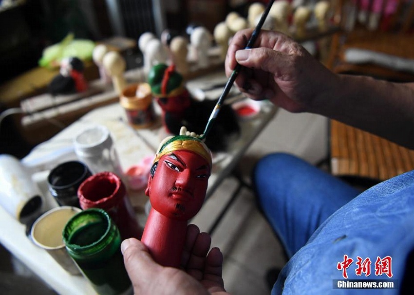 アトリエで木彫り人形の頭に色付けをする楊亜州さん（7月1日、撮影・張斌）。