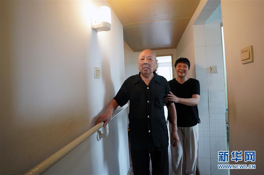 北京市朝陽区常営地区民族家園コミュニティにある自宅に新しく備え付けられた手すりにつかまって歩く、100歳になる哈雲成さん（写真左、2018年7月10日撮影）。