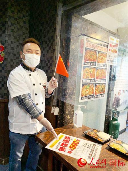 店内で中国の国旗を持ち、日本の現地の人々と共に新型コロナウイルスと闘い、困難を乗り切ろうという思いを示す李さん（画像は李さんが提供）。