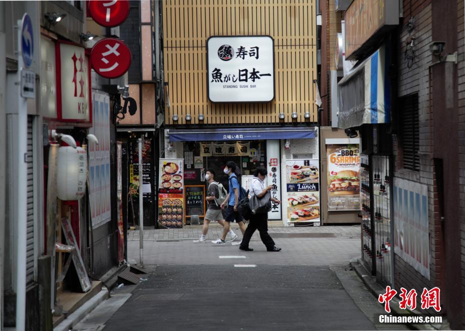 東京で、すし屋の前を通り過ぎる市民（撮影・呂少威）。