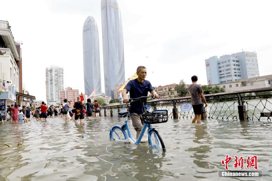 潮位が上昇して冠水した沙坡尾歩道を自転車を押しながら移動する市民（撮影・李思源）。