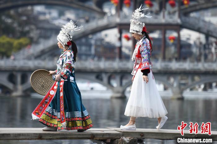 ミャオ族の民族衣装姿で木製の橋を渡る観光客（撮影・楊華峰）。