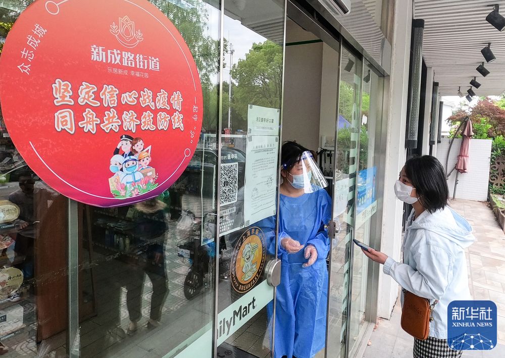 上海市嘉定区新成路街道（エリア）でQRコードをスキャンしてコンビニに入店する人（写真右）。同エリアではコロナ感染対策基準を満たすと認定された商店などに赤い円形のシールを掲示している（5月9日撮影）。