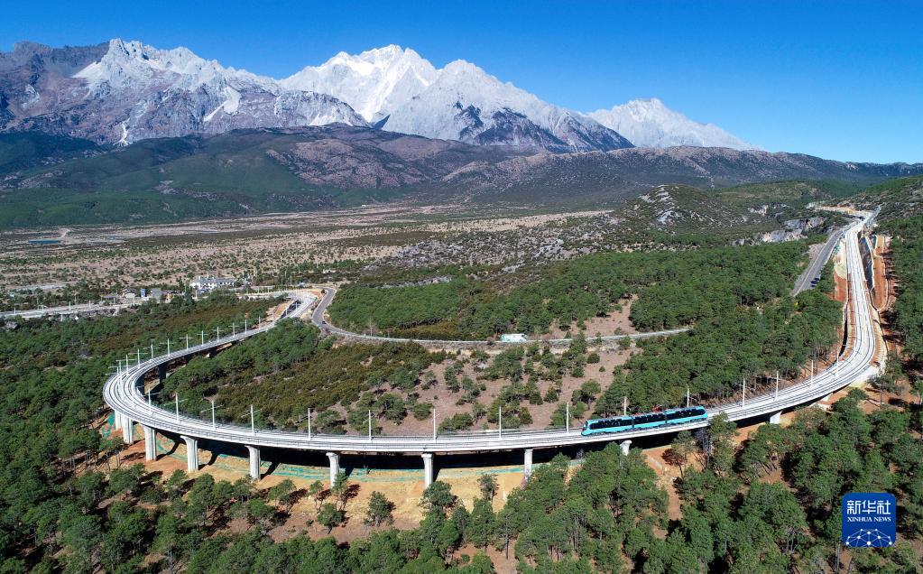 「麗江観光列車」プロジェクト（第1期）線の東巴谷一号大橋を走行する観光列車。遠くには玉竜雪山が見える（11月28日ドローンによる撮影・陳欣波）。