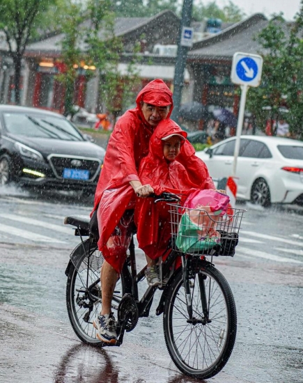 7月30日、自転車に子供を乗せ、合羽を着て雍和宮大街を通る男性。撮影・陳鍾昊