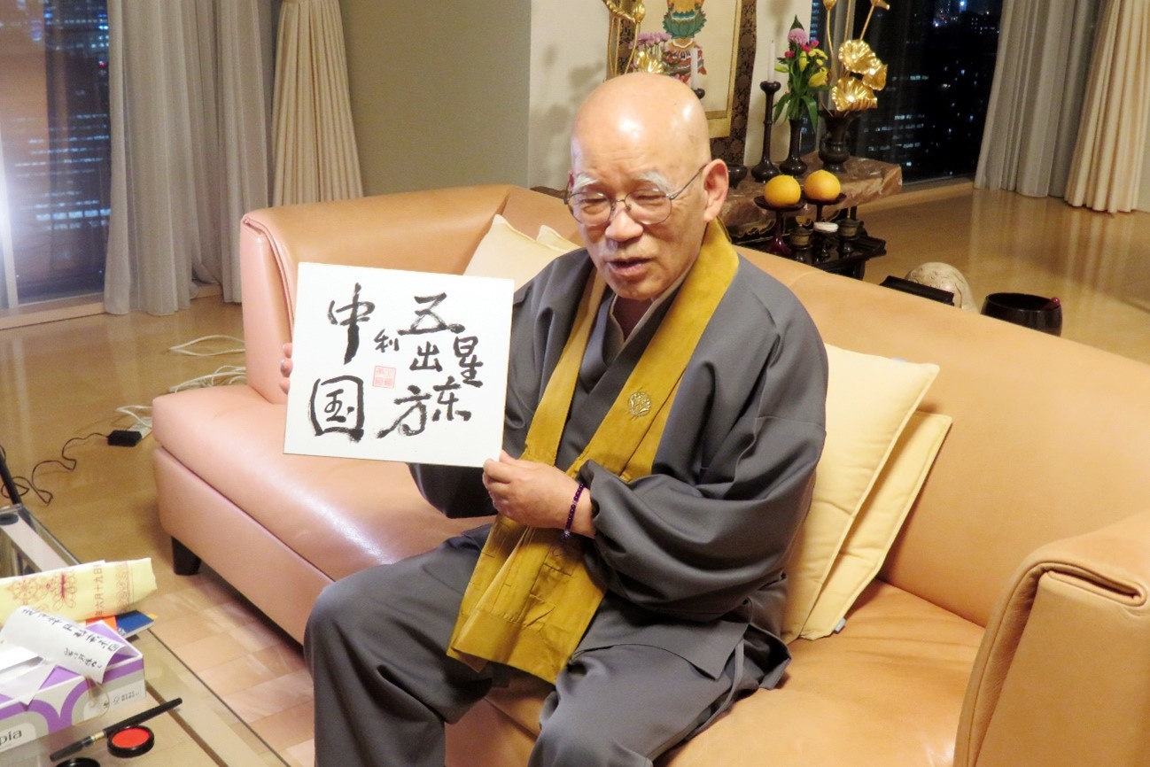自ら書いた「五星出東方利中国」を見せる小島康誉氏（画像は動画のスクリーンショット）。