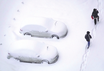 煙台市で雪にすっぽり埋まってしまった車の横を通る市民。