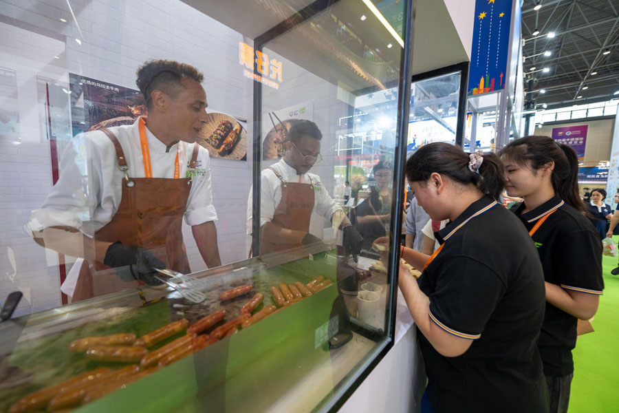 高級食品・サプリメント展示エリアで、ウルグアイの牛肉ソーセージを試食する来場者（撮影・翁奇羽）。