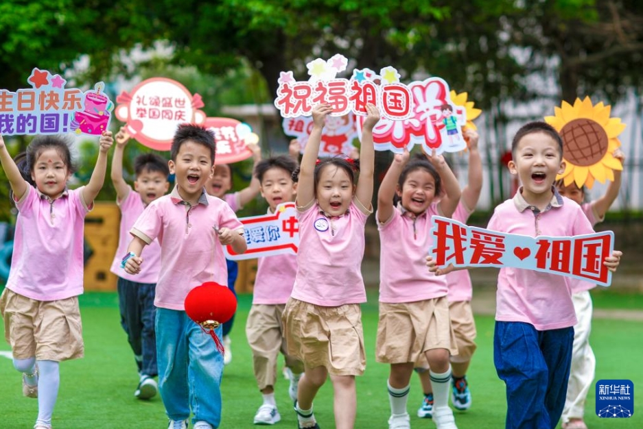 江蘇省興化市の四牌楼幼稚園で、国慶節を祝うメッセージボードを手に走る園児（9月26日撮影・周社根）。