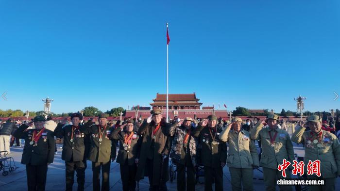 10月26日、天安門広場に掲げられた国旗の前で記念写真を撮影する抗米援朝出国作戦に参加した老兵(撮影・劉子衿)。