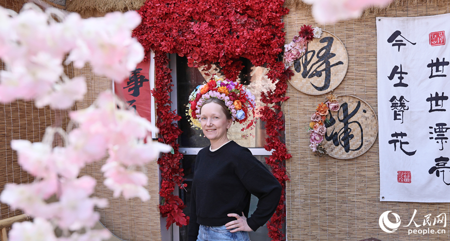 「簪花圍」で飾り立て、ドアの前で笑顔でポーズを付ける外国人観光客（撮影・李昌乾）。