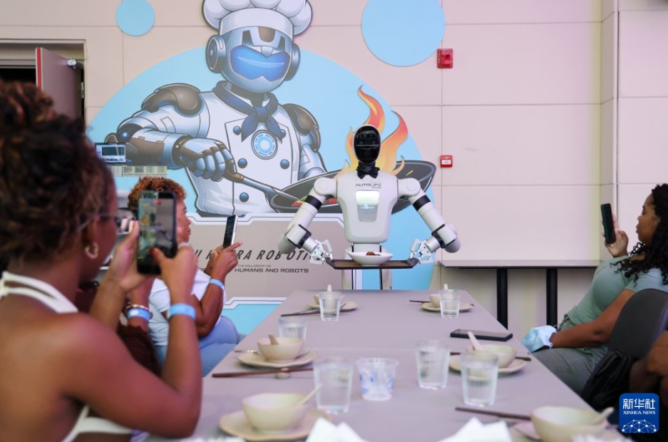 深セン市竜崗区にある世界初のロボット6S店（販売・部品・サービス・情報フィードバック・レンタル・カスタムメイドというロボットのライフサイクル全体をカバーするサービスを提供する店）の店内レストランで、料理を運んできたロボットをスマホで撮影するジャマイカ人観光客（8月4日に撮影・梁旭）。