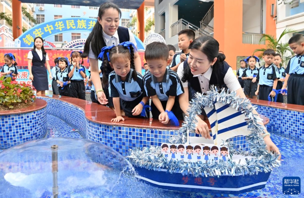 広西壮（チワン）族自治区南寧市にある浜湖路小学校教育集団浜湖校区で行われた「長征の道を歩み 中国の夢を共に築く―長征勝利90周年記念と2026年秋学期最初の思想政治教育授業」テーマ活動で、「夢の船」を水に浮かべた教員と児童（8月31日撮影・陸波岸）。