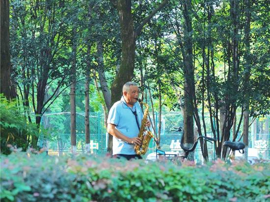 街路樹が茂る道でサックスを演奏する男性（撮影・付玥玥）。