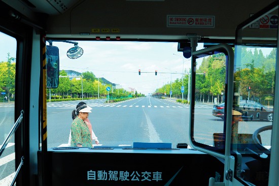 赤信号で自動で停車したB19自動運転バスの前を歩く歩行者。