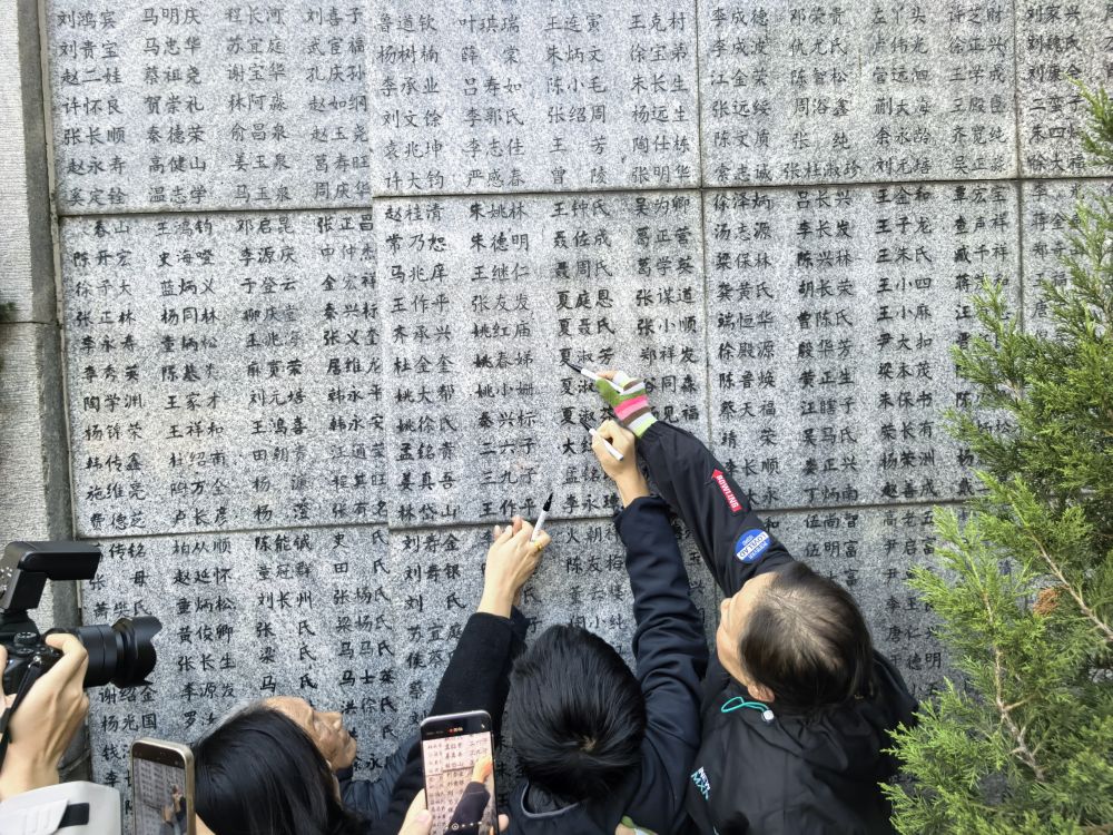 「嘆きの壁」に刻まれた親族の名前を指す南京大虐殺の生存者・夏淑琴さん。その横で名前を塗りなおす娘とひ孫(撮影・邱氷清)。